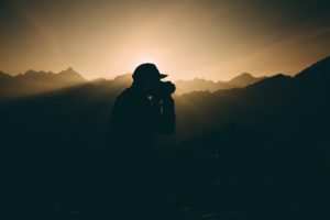 This is a silhouette photograph of a photographer photographing a scenic view.